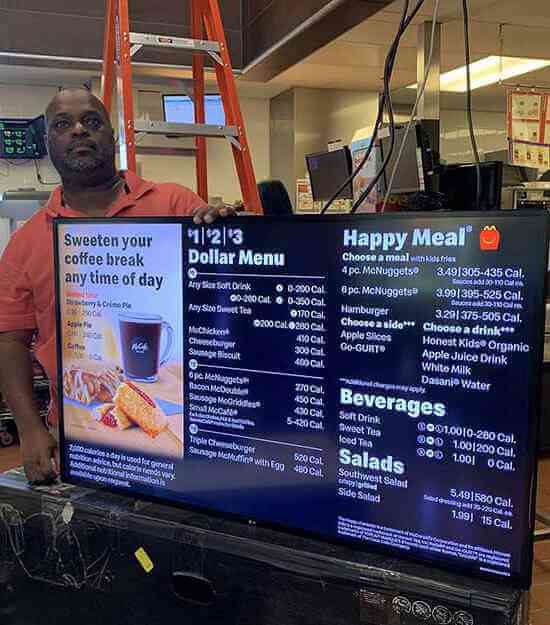 A man standing in front of a large TV displaying a McDonald's menu board